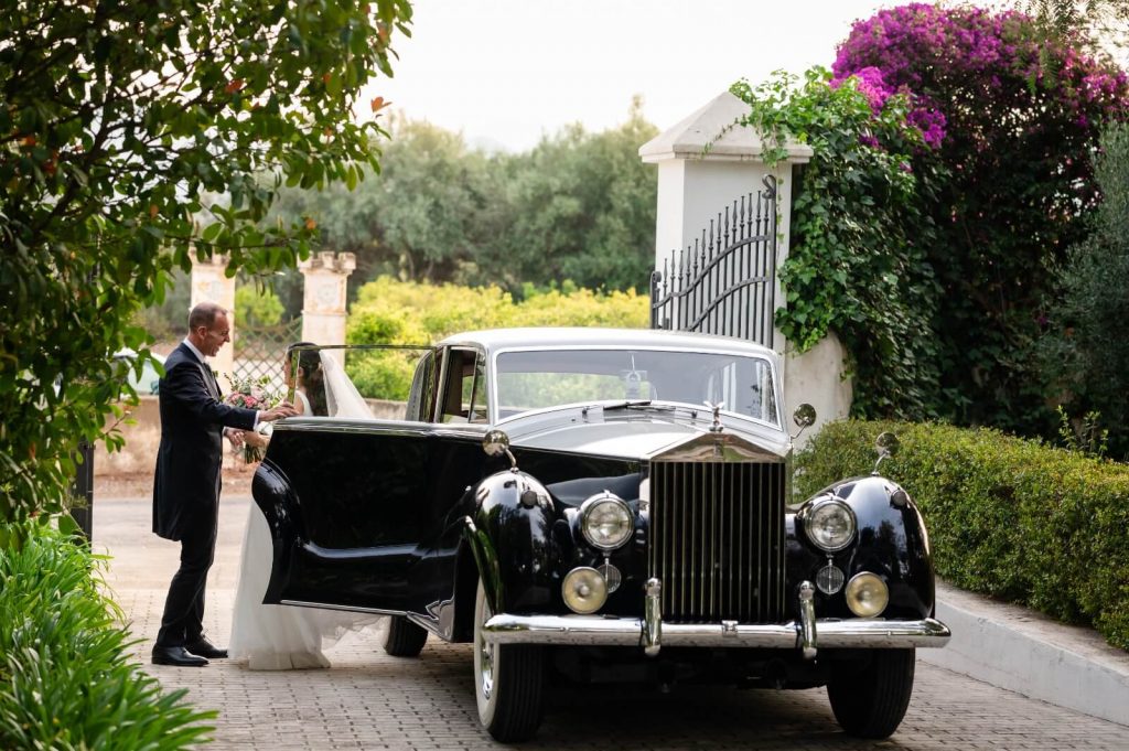 Novia y novio junto al Rolls Royce con ramo de flores